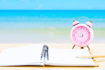 book and vintage clock with yellow on wooden platform beside tropical beach and blue sea on day...
