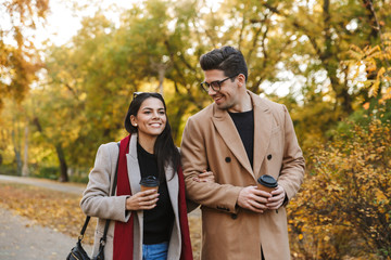 Portrait of european couple drinking takeaway coffee from paper cups while walking in autumn park