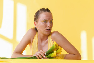 Young beautiful woman with the face of freckles wearing in yellow dress near background with afternoon shadows.