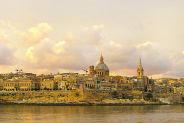 Obraz na płótnie Canvas Skyline at beautiful sunrise from Sliema with churches of Our Lady of Mount Carmel and St. Paul's Anglican Pro-Cathedral. Panoramic view of Valletta city - the Capital of Malta.