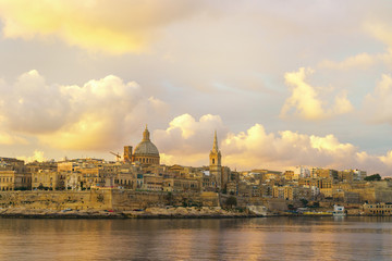 Fototapeta premium Valletta morning skyline with Basilica of Our Lady of Mount Carmel as seen from Sliema, Malta. Green plants landscape design garden foreground. Horizontal summer background or wallpaper.