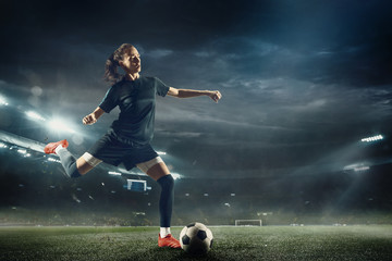 Fototapeta na wymiar Young female soccer or football player with long hair in sportwear and boots kicking ball for the goal in jump at the stadium. Concept of healthy lifestyle, professional sport, hobby, motion, movement