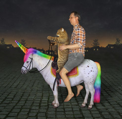 The barefoot man with his cat is riding together on the real unicorn  along a cobbled road at night.