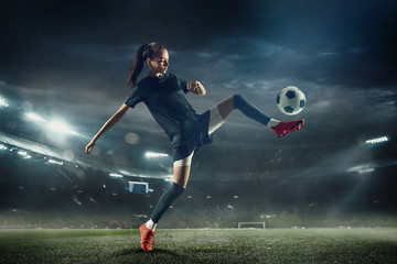 Obraz na płótnie Canvas Young female soccer or football player with long hair in sportwear and boots kicking ball for the goal in jump at the stadium. Concept of healthy lifestyle, professional sport, hobby, motion, movement