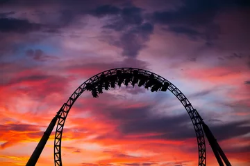 Fotobehang Amusementspark Silhouet van mensen die plezier hebben op een achtbaan in een pretpark bij zonsondergang. Adrenaline-concept.