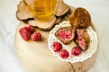 Chocolate candy truffle with raspberry on a wooden stand with glass of green tea. Close-up.