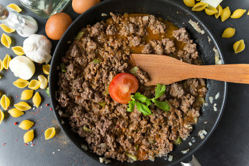 meat gravy with tomato in a pan , wooden spatula, shell paste, eggs, garlic, onion, spices, butter, top view