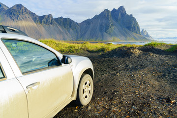 Fototapeta na wymiar Dirty silver color car on countryside road in Vesturhorn Mountain in summer morning. Stokksnes, Iceland, Northern Europe, Scandinavia. Scenic beautiful nature landscape. Popular tourist attraction.