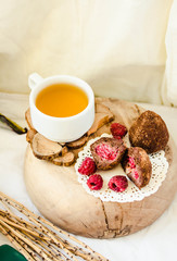 Served chocolate balls pralines with fresh berries in the green plate on white linen tablecloth backgound. A cup of herbal tea and glass of Cocoa powder.