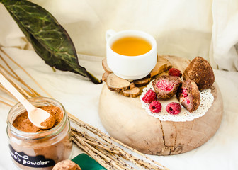 Served chocolate balls pralines with fresh berries in the green plate on white linen tablecloth backgound. A cup of herbal tea and glass of Cocoa powder.