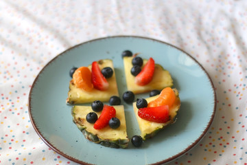 Plate with pineapple 'pizzas' - slices of pineapple with strawberries, tangerines and blueberries. Selective focus.