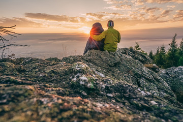 Two people in sleeping bag sitting on the rock watching sunset or sunrise. Romantic view from...