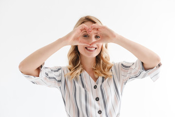 Portrait of positive blond woman smiling at camera while showing heart shape with fingers