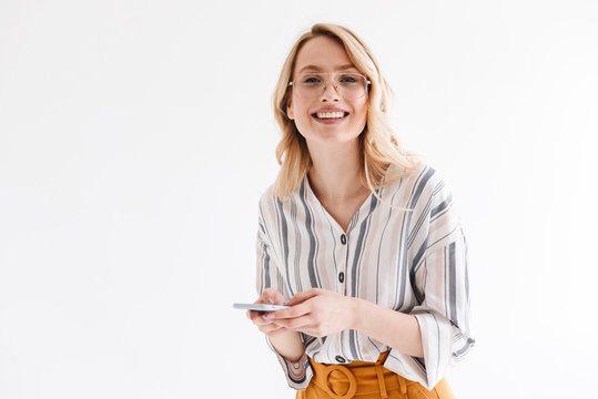 Photo of optimistic beautiful woman wearing glasses smiling at camera and typing on smartphone