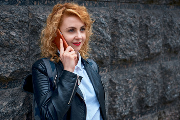 curly blonde young woman emotionally talking on a cell phone near a stone wall
