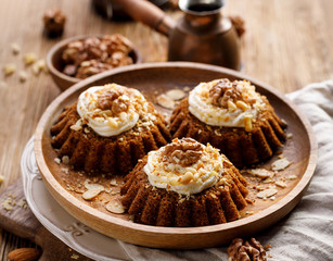 Carrot-nut muffins with mascarpone cream decorated with walnuts, pine nuts and cinnamon on a wooden plate. Delicious dessert