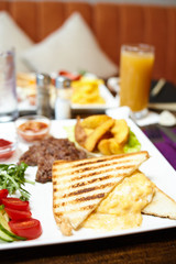 Breakfast meal - sandwich with scrambled egg, potato and steak with salad - image. Blurred background