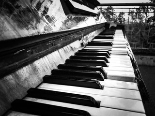 Black and white photo of the keys of an old broken street grand piano. Tragic photo with the mood of street music. Contrasting black and white keys of a street piano.