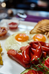 Food macro photo closeup - fried sausages, fried eggs with toast and ketchup. Table setting, blurred background - image