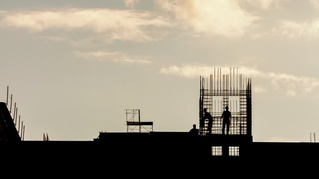 Silhouette of construction workers working on construction site, constructors working with steel rebar on residential building sunny evening, golden hour, warm cloudy sky time lapse, moving clouds