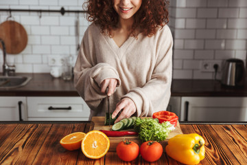 Photo of happy young woman cutting fresh vegetables while cooking salad at home