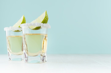 Golden mexican alcohol drink tequila with slice lime, salt on edge in shot drink on  green color background, white wood board.
