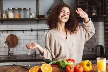 Image of happy young woman smiling while cooking salad with fresh vegetables at home