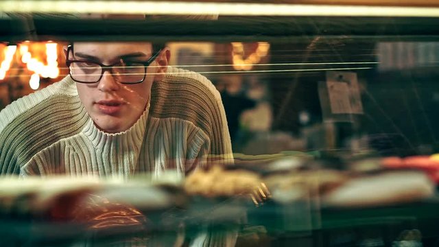 man choosing cakes incoffee shop. Shoot through the glass, glare and reflections on glass