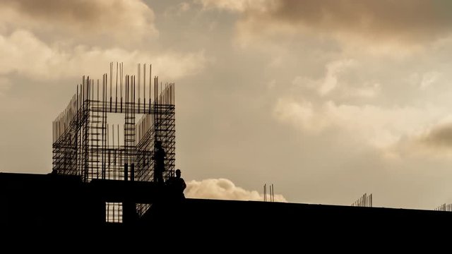 Silhouette of construction workers working on construction site, builders working with steel rebar on residential building sunny evening, golden hour, warm cloudy sky time lapse, moving clouds