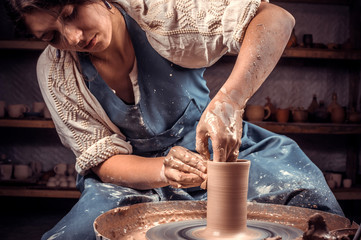 Charming ceramist woman shows how to work with clay and pottery wheel. Making ceramic dishes.