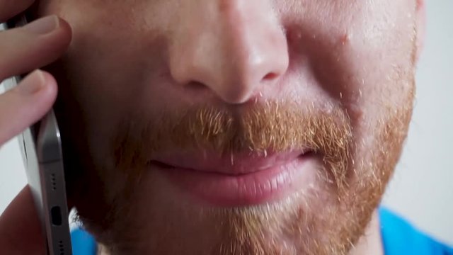 Close up of a young bearded ginger man speaking on the phone and laughing