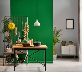 cooking utensils in front of the green wall, pot, wood fork and spoon, cutting board, chair lamp and frame style.