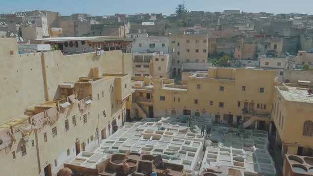 Overlooking the famous Tannery in Fez, Morocco with stone vessels filled with a colorful dyes as a historical tradition to dye materials panning through a metal fence with transitions at the end