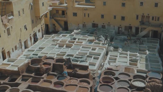 Overlooking the famous Tannery in Fez, Morocco with stone vessels filled with a colorful dyes as a historical tradition to dye materials panning through a metal fence