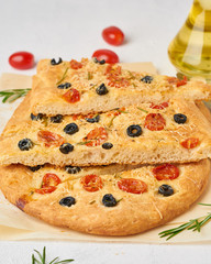 Focaccia, pizza, chopped italian flat bread with tomatoes, olives and rosemary. Vertical, side view.
