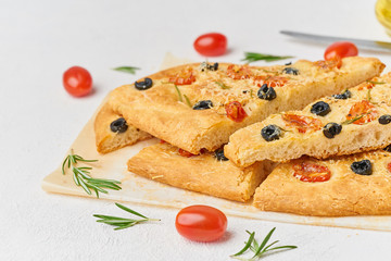 Focaccia, pizza, sliced italian flat bread with tomatoes, olives and rosemary. Side view, copy space