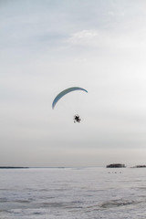 Paraglider with motor flies over the sea, which is covered with ice and snow. Free flight in winter
