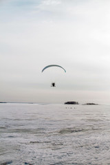 Paraglider with motor flies over the sea, which is covered with ice and snow. Free flight in winter