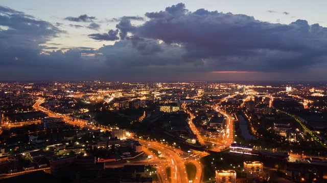 Top view of evening city, drone time lapse street roads traffic, illuminated avenue crossroad car light trails at night. cityscape on horizon, rolling clouds after sunset