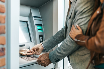 Obraz premium Senior father and his daughter using atm machine together to withdraw money. They are happy. Bright sunny day.