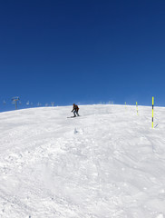 Skier downhill on snowy ski slope in sunny winter day