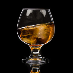 A round glass of whiskey brandy with ice, a wave and a small splash
