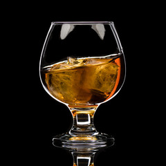 A round glass of whiskey brandy with ice, a wave and a small splash