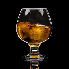 A round glass of whiskey brandy with ice, a wave and a small splash