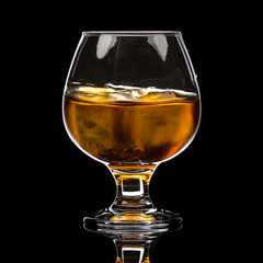 A round glass of whiskey brandy with ice, a wave and a small splash