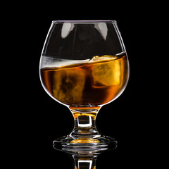 A round glass of whiskey brandy with ice, a wave and a small splash