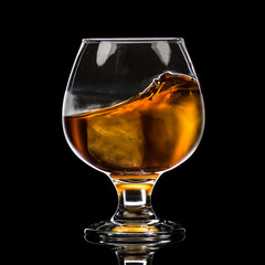 A round glass of whiskey brandy with ice, a wave and a small splash