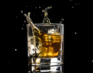 Hexagonal glass of whiskey brandy with ice and splashes from falling ice