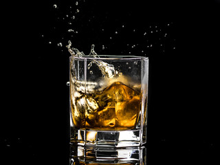 Hexagonal glass of whiskey brandy with ice and splashes from falling ice