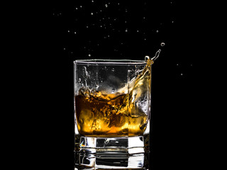 Hexagonal glass of whiskey brandy with ice and splashes from falling ice